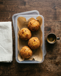 Four arancini in a takeaway container with an espresso cup for size reference