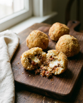 Four homemade arancini ragù with golden breadcrumb coating, one cut open